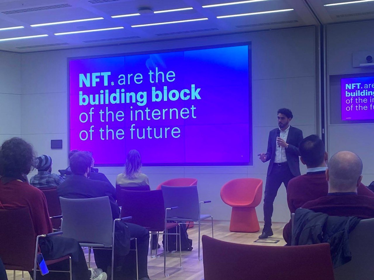 Speaker on stage beside a slide: NFTs are the building block of the internet