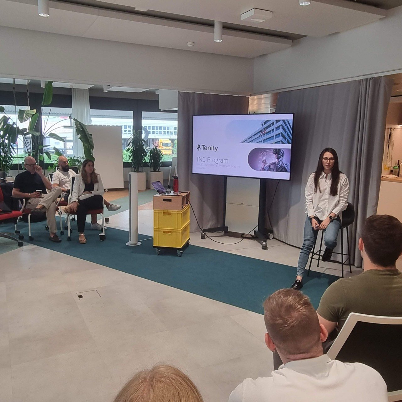 Presenter at the Tenity INC Program event, with a panel seated beside the screen